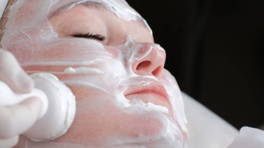 Tam bir kadının yüzüne bir yordam üzerinde Close-up. Profesyonel bir güzellik uzmanı beyaz eldiven eller kadın yanağına bir ultrason makine yardımı ile kırışıklıkları düzeltmek.