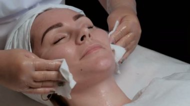 Yüz Nemlendirici ve güzellik salonunda cilt temizleme prosedürü güzel bir kız. Bir kadın s boyun, çene, alın, burun ve yanak beyaz peçete ile bir güzellik uzmanı losyonları.   