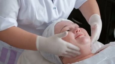 Nemlendirme ve güzellik salonu yüzüne temizlik kadın prosedürü. Boyun, çene, alın, burun ve kozmetik ofiste bir gülümseyen kız yanakları Şevval özçelik güzellik beyaz eldiven sabunlar.