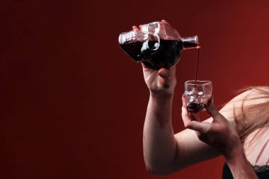 Kız bir kafatası şeklinde bir bardak içine şarap ya da bir şişe kan döker. Cadılar Bayramı kutlama kavramı. Yakın çekim. Uzay kopyalayın. Kırmızı bir arka plan.