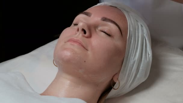 一个年轻的女人躺在她的眼睛关闭在一个医疗美容店的皮肤清洁程序 美容师的手在透明手套肥皂的脸上一个美丽的性感的欧洲女孩 — 图库视频影像