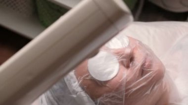 Kavram. Sağlık ve güzellik. Gözenekleri genişleterek ve cildi buharlama için tedavi Kosmetoloji yordamı. Sıcak buhar bir kadın kozmetik ofiste çehresini yönlendirilir. Kamera hareket.