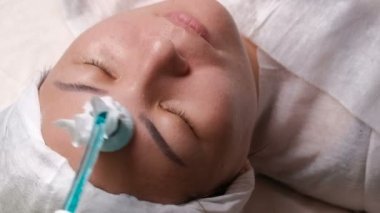 Darsonvalization. Fizyoterapi yüz gençleştirme yordam Müslüman bir kadının çehresini Close-up. Bir güzellik uzmanı elinde bir aygıtı yüksek frekanslı pulsed alternatif akımları ile kullanın. Kan dolaşımı, geliştirilmesi aktivasyonu