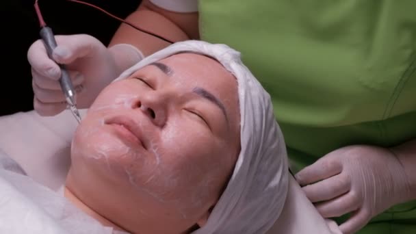 Cosmetología de hardware. Una mujer musulmana con los ojos cerrados sonríe durante un procedimiento de desincrustación terapéutica. Primer plano. Chica oriental en la limpieza galvánica de la piel en el salón de belleza . — Vídeo de stock