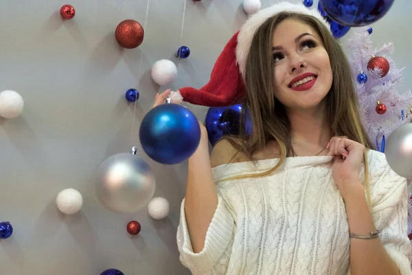 新しい年のテーマ 白地に青と赤のクリスマス ボール 側に見えるニットのセーターの若い美しいセクシーな髪の長い女の子の肖像画 — ストック写真