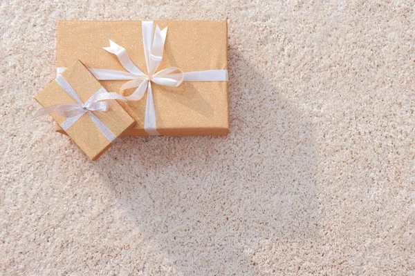 Golden paper, holiday, delivery, gifts, surprise. Boxes tied with white tape of different sizes lie on the rug in the upper left.