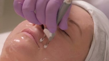 Elektrikli bir cihaz kullanarak yüz masajı için kozmetik prosedür. Güzellik uzmanı'nın Close-up mor eldivenler elektrotlar yardımıyla Yumuşak kırışıklıkları eller..