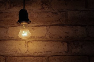Bir tuğla duvar arka plan üzerinde ampul parlak. Enerji tasarrufu kavramı. Sıcak arka planda karanlık bir anahtar, bodruma benzer.