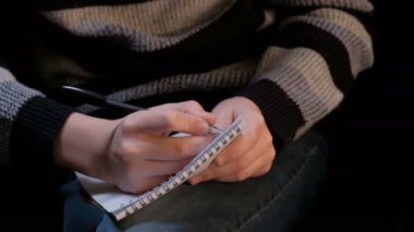 Bir not defteri ve siyah tükenmez kalem olan genç bir adam elinde closeup. Adam yazmak bir şey, ama düşünmek veya alamaz karar vermek istiyor. Defter öğrencinin tur bir kafeste.