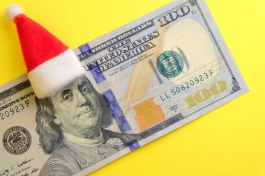 Kırmızı Santa Claus şapka Franklin'in başına 100 dolar. Ne kadar para insanlar kış tatil günlerinde harcamak. Finansal borç olmadan yeni yılda. Sarı arka plan.