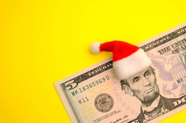 Lincoln ün başına 5 dolar üzerinde kırmızı Santa Claus şapka. Sarı arka plan kopya alanı ile. Finansal borç olmadan yeni yılda. Ne kadar para insanlar kış tatil günlerinde harcama yapmak.