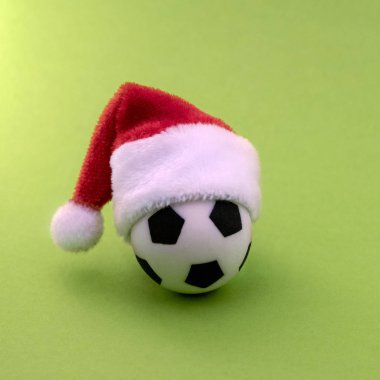 Hediyelik eşya futbol topu yeşil bir arka plan üzerinde kırmızı bir Noel Baba şapkalı. Spor Noel hediyesi kavramı. Yeni yılda futbol zafer sembolü. Kare kare. Kopya alanı.