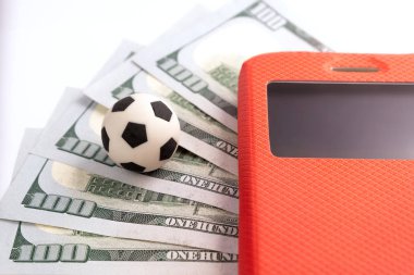 Bir futbol topu beş yüz üzerinde bize dolar kırmızı durumda hareket eden telefon yanında yatıyor. Yakın çekim. Spor bahisleri kavramı.