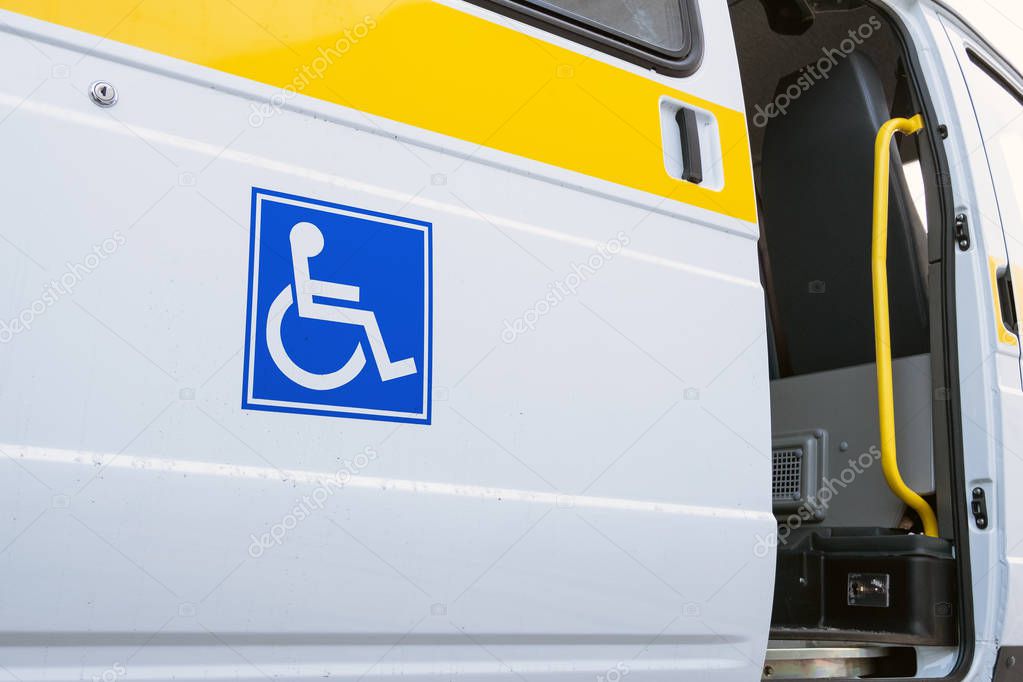 White bus with a blue sign for the disabled. The open door of a specialized vehicle for people with disabilities. Yellow bar and handrail.