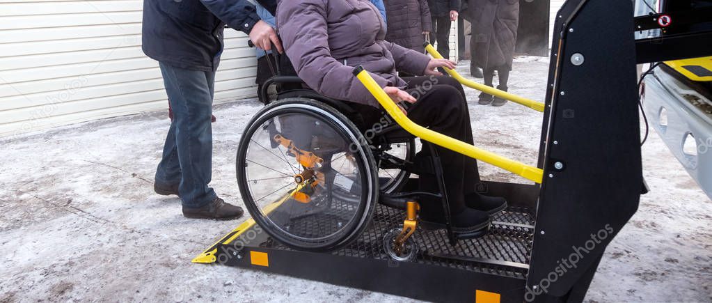 Winter. A woman in a wheelchair on a lift of a specialized vehicle for people with disabilities. Taxi for the disabled. Yellow bar and handrail.
