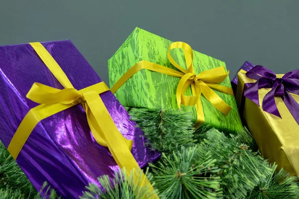 Cajas de regalo púrpuras, verdes y doradas en las ramas del árbol de Navidad sobre un fondo gris. Fondo conceptual para el diseño de las vacaciones de Año Nuevo . —  Fotos de Stock