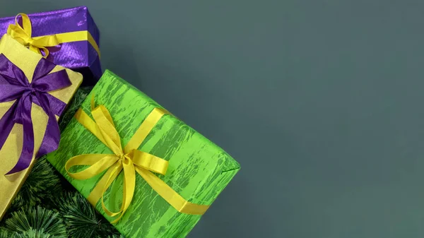 Cajas de regalo en las ramas del árbol de Navidad sobre un fondo gris. Embalaje violeta, verde y dorado. Copiar espacio. Fondo conceptual para el diseño de las vacaciones de Año Nuevo . —  Fotos de Stock