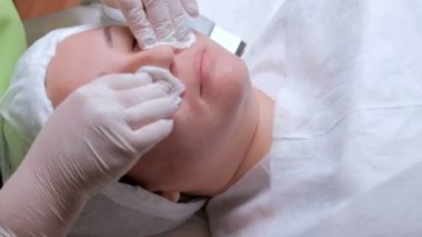 Güzellik uzmanı veya laboratuvar asistanı olarak beyaz eldiven eller bir kadının yüzüne Pamuklu ped ile silin. Asyalı bir kadın kozmetik veya tıbbi prosedür için hazırlanıyor.