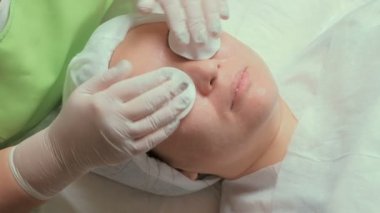 Relax beyaz eldiven Pamuklu ped ile bir Asyalı kız gözlerini kapatır. Gençleştirici bir uygulama veya bir güzellik salonu maskede Temizlik Kozmetik prosedür. Eller closeup.