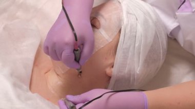 Orta yaşlı kadın kozmetik kliniğinde bir resepsiyonda kapalı gözlerle. Lila eldiven güzellik uzmanı'nın elinde iki elektrot yardımıyla istemcinin boynundaki Microcurrent masaj olun. Donanım kozmetik. Yakın çekim.