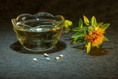 Aspir boyama, Carthamus tinctorius, Amerikan safran, vahşi thistle. Sarı renk, tohum ve yağ bir cam fincan koyu kumaş üzerinde kuru çiçek ışık parlak bir nokta tarafından vurgulanır. Antik Mısır zamanlardan beri yağlı tohum ve boyama, kültür.