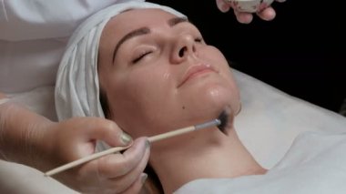 Güzellik salonu ya da kozmetik merkezi yüzüne cilt temizliği için yordam. Krem güzel bir kızın yanaklarda yayılan bir kozmetik fırça Close-up. İşlenmemiş video.