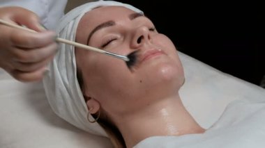 Profesyonel Şevval özçelik güzellik güzellik salonunda kadın boyun kozmetik maske uygulanıyor. Şeffaf bir jel kozmetoloji merkezi istemcisinde yüzünde bir fırçayla uygulamak için yordamı.