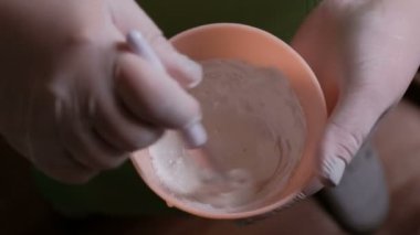 Malzemeler bir pembe kauçuk Kupası'nda karıştırma işlemi. Bir güzellik veya laborant beyaz eldiven yakın çekim çözüm bir fırça ile karıştırın. Güzellik salonu ya da tıbbi laboratuvar.