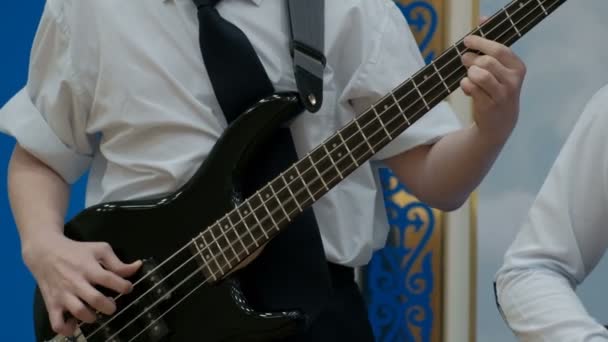 一个穿着白色衬衫的少年卷起袖子演奏一把电动低音吉他 右手的手指在牵线搭桥 青年的概念音乐主题 — 图库视频影像