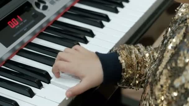 Teen κορίτσι σε μια λαμπερή χρυσή μπλούζα παίζει το ηλεκτρικό πιάνο. Παιδικά δάχτυλα, πατήστε τα πλήκτρα του συνθέτη. Επιδόσεις συναυλία. Αντίληψη για το θέμα των νέων μουσικών. — Αρχείο Βίντεο