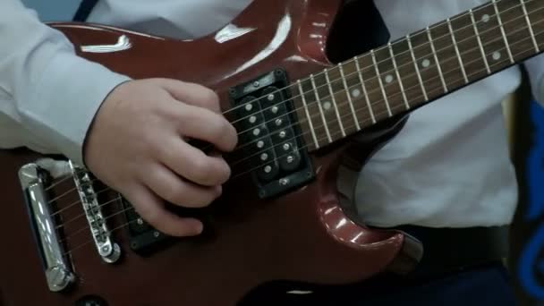 Close-up dos dedos de um adolescente tocando uma guitarra elétrica marrom. O tipo puxa os cordelinhos numa ferramenta de poder musical. Conceito tema musical da juventude . — Vídeo de Stock