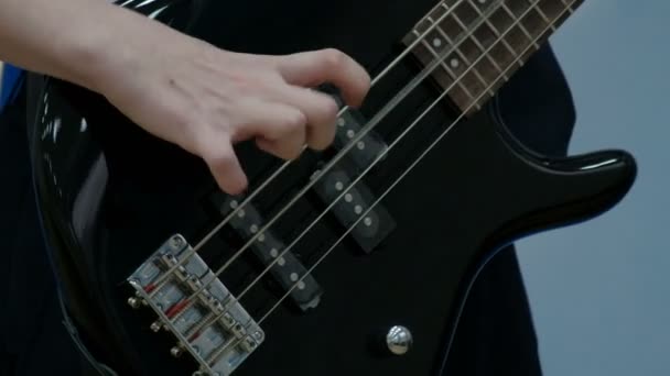 Nahaufnahme der Finger eines Teenagers, der eine schwarze E-Bass-Gitarre spielt. der Kerl zog die Saiten an einem musikalischen Elektrowerkzeug. Konzept Musikalisches Thema der Jugend. — Stockvideo