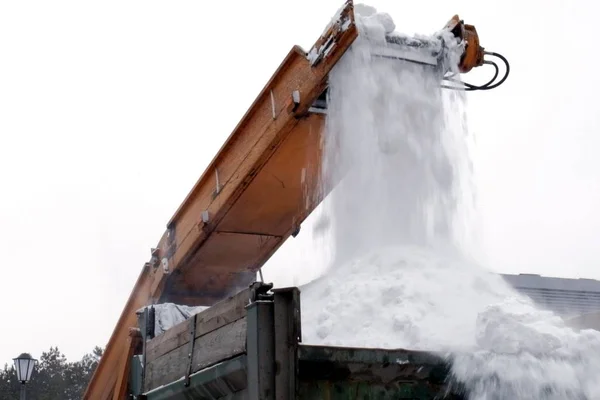 Winter. Municipal urban road maintenance. Cleaning of heavy snow on the streets of the city. Close-up of falling snowballs in a truck from a snow removal vehicle.