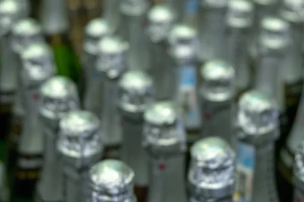 Blurred. Rows of bottles in a warehouse or supermarket. Abstract background of bottlenecks with wine or champagne.