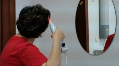 Tarak darsonval. Kırmızı gömlekli bir kadın saçlarını bir ayna önünde ile elektrikli bir cihaz araması yapıyor. Cilt tıbbi prosedür.