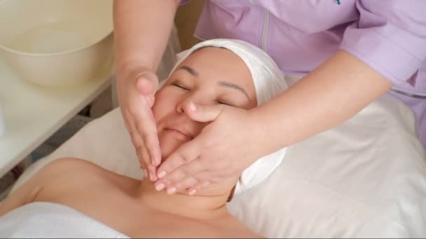 Asiatisches Mädchen über den Eingriff im Schönheitssalon. Massage, Verjüngung und Reinigung der Haut. die Hände der Kosmetikerin waschen die Kundin mit Seifenlauge. — Stockvideo
