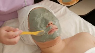 Profesyonel bir Kozmetolog, görünümdeki yetişkin bir kadının yüzüne bir aljinat maskesi uygular. Bir spa salonunda Müslüman bir kız için gençleştirici prosedürü. Renk düzeltmesi olmadan RAW video.