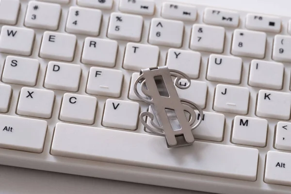 Clip d'argent en métal sous la forme d'un symbole de dollar américain. Partie d'un clavier d'ordinateur blanc. Le concept d'entreprise sur Internet, freelance, revenus PC, investissements en ligne et risques . — Photo