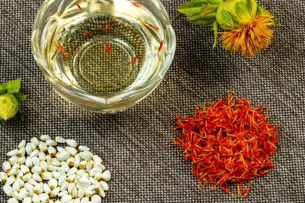 Safflower. Oil, seeds, bud, flower, red inflorescences of wild saffron. Close-up, gray fabric background. Ingredients for health, cosmetology and paint. — Stock Photo, Image