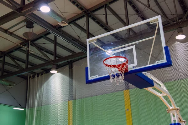 Schlecht gewaschenes Glas-Basketballbackboard mit einem Korb in einem Sportkomplex. Grüner Hintergrund. Sportthema. Kopierraum. Laternen an der Decke. — Stockfoto