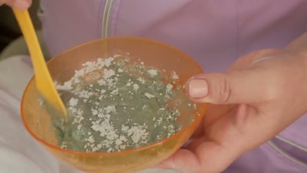 Närbild. Professionell kosmetolog blandar ingredienser i en orange cup. Beredning av en blandning för att tillämpa alginat anti-aging mask på ansikte och kropp av kvinnor. — Stockvideo