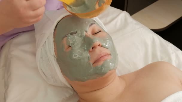 Närbild. Kosmetiska förfarande för tillämpning av alginat mask på framsidan en östlig asiatisk kvinna. En professionell kosmetolog omfattar patienter ögonen med en grå massa. Skönhet, hälsa och mode. — Stockvideo