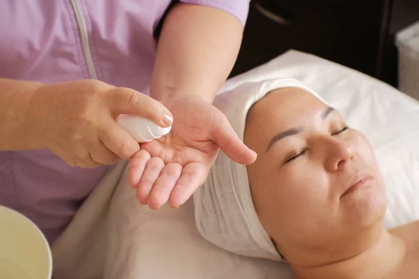 Schoonheidsspecialiste smeert de handen met een gel toe te passen op het gezicht van een vrouw. Voorbereiding voor cosmetologie procedures in een schoonheidssalon. Close-up. Schoonheid. Cosmetologie. Gelaatsverzorging — Stockfoto