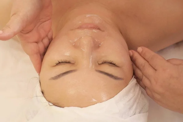 Közelről. Portréja egy nő az ázsiai megjelenést kap a Wellness masszázs az arcon. Egy nő csukott szemmel fekszik a kozmetikus a kanapéra. A fenti felvétel — Stock Fotó