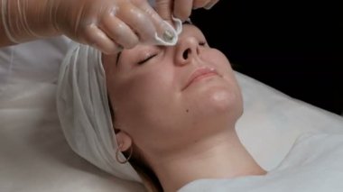 Güzellik salonunda güzel bir kızın portresi. Bir kozmetolojist-terapist müşterinin yüzünü siler. Kırışıklıkları azaltmak ve kadın cilt gençleştirme için prosedür. Close.