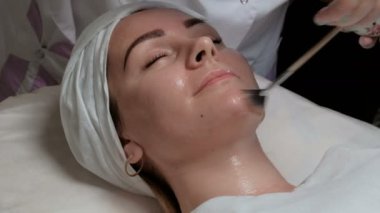 Güzellik salonunda prosedür üzerinde güzel bir kız portresi. Close. Bir kozmetolojist-terapist kırışıklıkları azaltmak ve kadın cilt gençleştirmek için müşterilerine yüz şeffaf bir jel uygular.