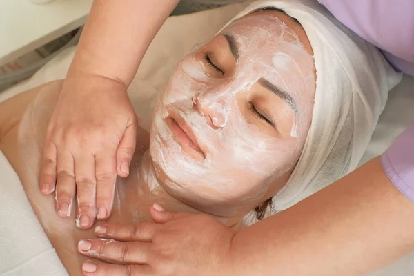 Un cosmetologo massaggia il viso e il collo di una donna con una maschera idratante. Primo piano. Donna asiatica rilassata prende trattamenti di bellezza nel salone di bellezza. Cosmetologia. Bellezza — Foto Stock