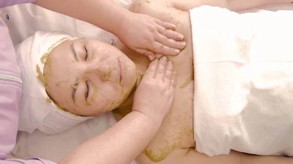 Aziatische vrouw nemen spa-behandelingen in de schoonheidssalon. Schoonheidsspecialiste masseert een vrouw gezicht met een masker van kiwi of groene algen. Dag van een professionele schoonheidsspecialist. Het concept van lichaamsverzorging. — Stockfoto