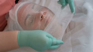 Şevval Özçelik Güzellik yeşil eldiven bir bandaj ile güzel bir kızın çeneni. Güzellik Salonu aljinat maskesi uygulamak için hazırlık. Kadın cilt gençleştirici yordamı.