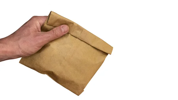 Mannenhand houdt een bruine papieren zak met inhoud. Geïsoleerd op een witte achtergrond. Kopieer ruimte. Het thema van het gebruik van milieuvriendelijke verpakking. — Stockfoto